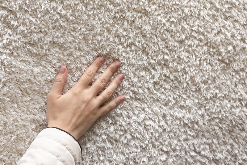 Soft looking hand gently feeling the soft texture of clean cream coloured carpet
